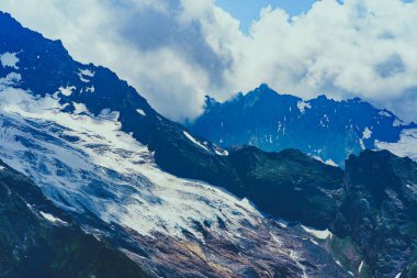 Yaz mevsiminde güzel bir dağ manzarası. Bulutlu havada karlı, kudretli dağlar.