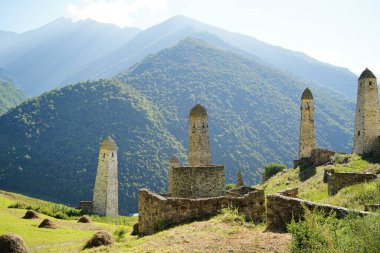 Yeşil dağlık arazide eski taş kuleler. Yeşil tepenin üzerindeki antik taş binalar yaz günü orman ve sisle kaplı dağlara karşı..