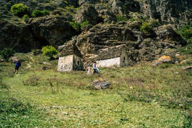 Yeşil dağlardaki antik taş evler. Güneşli yaz gününde, kayalık dağın yeşil çimenli yamacında yaşlanmış taş binalarla muhteşem bir manzara..