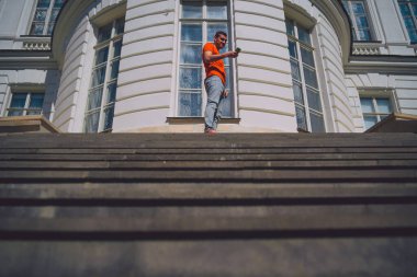 Genç adam cep telefonunu karıştırıyor, malikanenin merdivenlerinde duruyor. Sarayın merdivenlerinde güneşli havada akıllı telefonlu bir erkek turist dinleniyor.