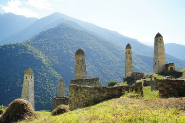 Yeşil dağlık arazide eski taş kuleler. Yeşil tepenin üzerindeki antik taş binalar yaz günü orman ve sisle kaplı dağlara karşı..