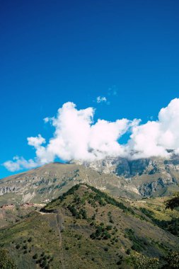 Resimli bir manzara var. Dağ bulutlu gökyüzüne karşı. Mavi gökyüzünde yüzen bulutlar dağ sırtı üzerinde