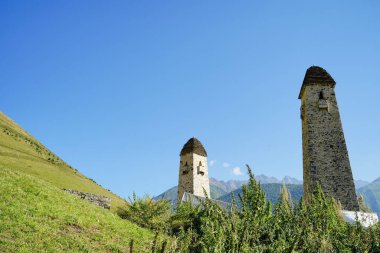 Yeşil dağlık arazide eski taş kuleler. Yeşil tepenin üzerindeki antik taş binalar yaz günü orman ve sisle kaplı dağlara karşı..
