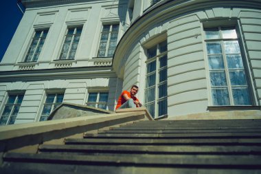 Genç adam başka tarafa bakıyor, malikanenin merdivenlerinde oturuyor. Sarayın merdivenlerinde güneşli havada poz veren erkek turist