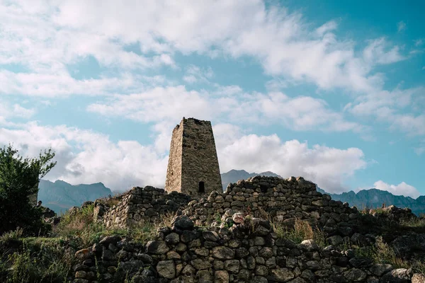 Old stone tower in green mountainous terrain. Ancient stone building of old town located on green hill against mountains covered with forest and fog in summer day.