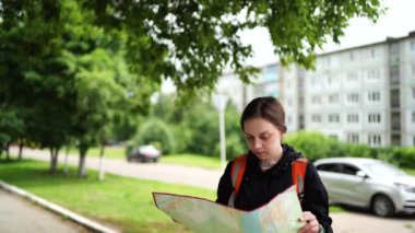 Sırt çantası ve haritası olan gezgin genç bayana yakın durun. Kadın turist okuma ve inceleme haritası, şehir caddesinde duruyor.