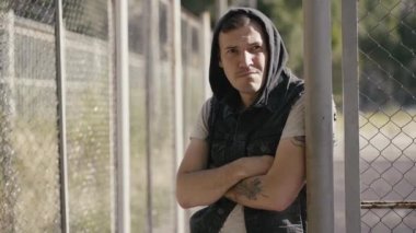 Çitin yanında duran kapüşonlu genç ve yakışıklı bir adam.  