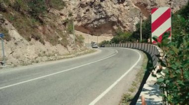 Dağlarda trafik işaretleri olan kıvrımlı bir yol. Kırmızı köşegen sol engelli trafik işaretini dağlık araziden geçen eğri asfalt yolun taştan sınırına koy