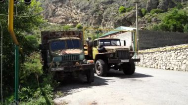 Kuzey Osetya, Rusya 1 Eylül 2020: Dağlarda kırsal yolda eski araçlar. Güneşli bir günde dağlık bölgede eski asfalt yolda park etmiş eski püskü kamyonlar.