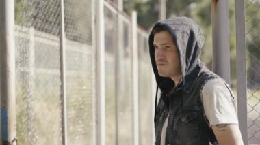 Çitin yanında duran kapüşonlu genç yakışıklı adam.  