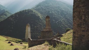 Yeşil dağlık arazide eski taş kuleler. Yeşil tepenin üzerindeki antik taş binalar yaz günü orman ve sisle kaplı dağlara karşı..