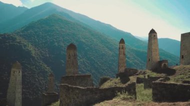 Yeşil dağlık arazide eski taş kuleler. Yeşil tepenin üzerindeki antik taş binalar yaz günü orman ve sisle kaplı dağlara karşı..