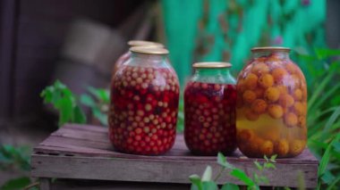 Kavanozlu kompot. Mühürlü cam kavanozlar ve kompot bahçedeki yaz günü çiçeklerin ve meyvelerin yanına konur..