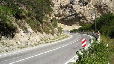 Dağlarda trafik işaretleri olan kıvrımlı bir yol. Kırmızı köşegen sol engelli trafik işaretini dağlık araziden geçen eğri asfalt yolun taştan sınırına koy