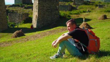 Tepede oturan genç adam. Hayalperest erkek yüksekte oturuyor ve parlak bulutlu gökyüzüne karşı konumlanmış muhteşem kayalıklara bakıyor.