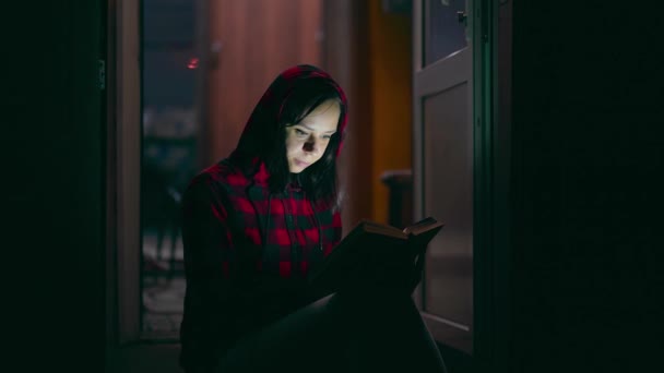若い女性がポーチに座って夜に本を読んでいます 大人女性休憩の本で新鮮な空気 楽しみます彼女の余暇 — ストック動画