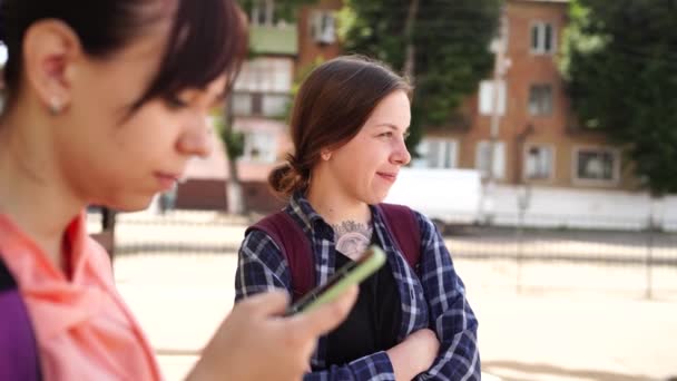 年轻女人闲聊着 站在街上 一个女人在看手机 另一个在讲什么 — 图库视频影像