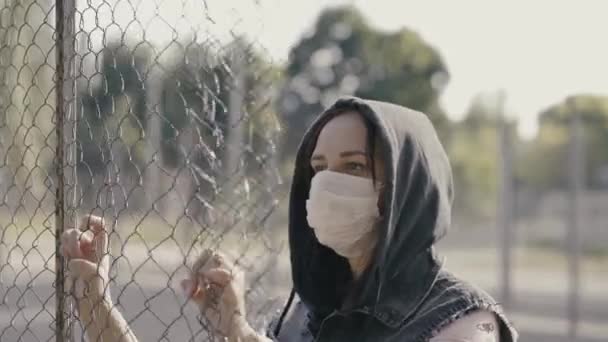 Kapüşonlu Tıbbi Maskeli Genç Kadın Portresi Güneşli Havalarda Çitleri Sallıyor — Stok video