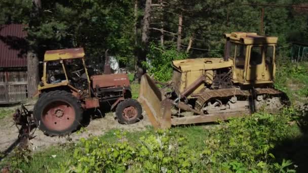 Vecchi veicoli in campagna. Trattore agricolo arrugginito e trattore cingolato parcheggiato in cortile in estate. — Video Stock