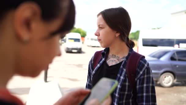 年轻女人闲聊着 站在街上 一个女人在看手机 另一个在讲什么 — 图库视频影像