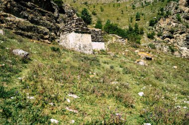 Yeşil dağlardaki antik taş evler. Güneşli yaz gününde, kayalık dağın yeşil çimenli yamacında yaşlanmış taş binalarla muhteşem bir manzara..