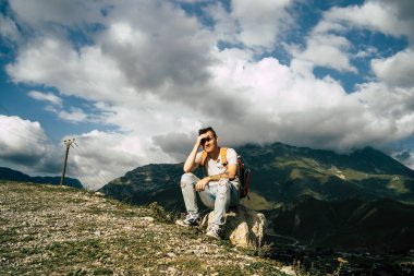 Yorgun bir seyyah tepede dinleniyor. Dağlarda aktif bir yürüyüşten sonra taşın üzerinde oturan bitkin erkek turist.