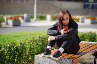 Park bankında oturan genç bir kadın, cep telefonuna bakıyor. Akıllı telefon kullanan bir kadın bir apartmanın avlusunda internet kullanıyor.