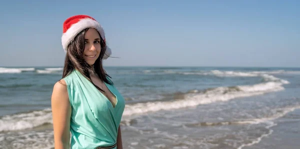海の近くでクリスマスを祝う女性 リゾートで波の海の近くに立っている間に笑顔クリスマスの帽子の喜びの女性 — ストック写真