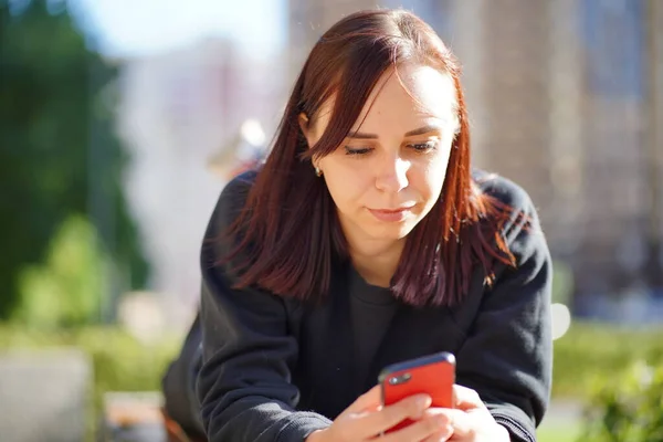 Egy Fiatal Fekszik Hasán Egy Padon Feltartott Lábbal Nézegeti Mobilját — Stock Fotó