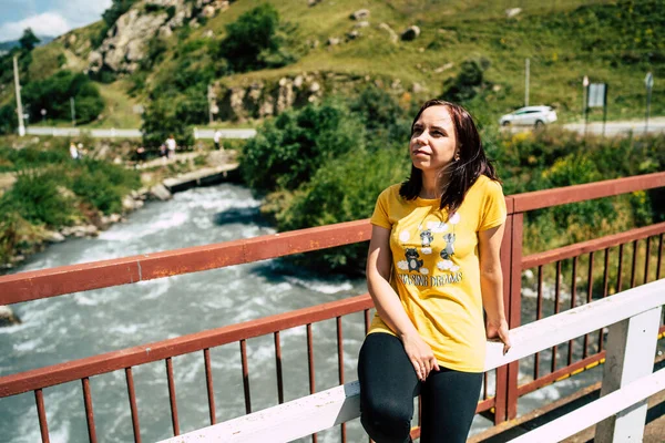 Kadın turistin bakışlarını başka yöne çevirin. Genç kadın güzel manzaranın tadını çıkarıyor, dağlık arazide köprünün üzerinde oturuyor..