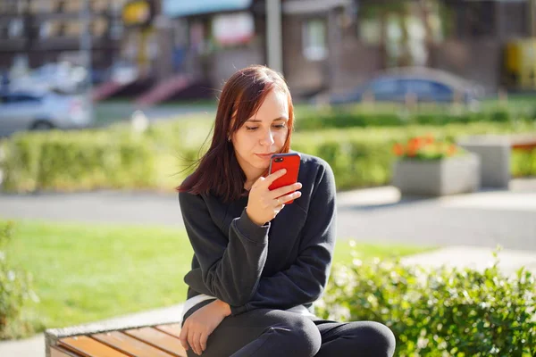 Jonge Vrouw Een Bankje Het Park Kijkend Naar Haar Mobiele — Stockfoto