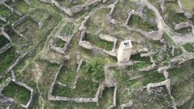 Yeşil dağlık arazide eski taş kuleler. Eski şehrin antik taş binaları dağlara karşı yeşil tepenin üzerinde yer alır.