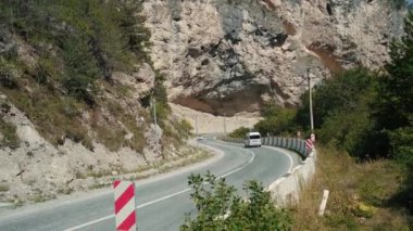 Dağlarda trafik işaretleri olan kıvrımlı bir yol. Kırmızı köşegen sol engelli trafik işaretini dağlık araziden geçen eğri asfalt yolun taştan sınırına koy