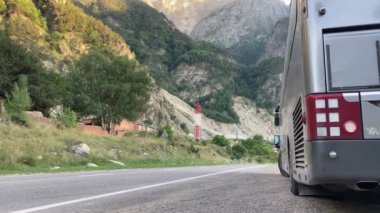 Büyük bir turist otobüsü dağ yolunda dışarıda duruyor.