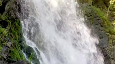 Dağ nehri taştan kıyıya doğru akıyor. Temiz su yolu güneşli havada taşların üzerinden akar..