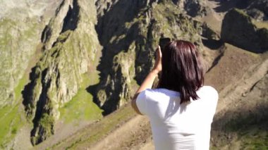 Genç bir kadın akıllı telefondan dağ manzarasının fotoğraflarını çekiyor. Dişi turist cep telefonuyla dağları fotoğraflıyor