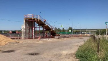 İnşaat işçileri güneşli bir yaz gününde yol üzerinde yaya inşa ediyorlar. İnşaatçılar, açık havada otoyolun yukarısından yaya geçişi yapıyorlar.