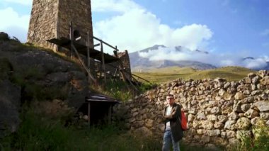 Dağlardaki eski harabelerin yanında duran bir gezgin. Sırt çantalı genç turistin yan görüntüsü