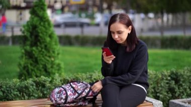 Park bankında oturan genç bir kadın, cep telefonuna bakıyor. Akıllı telefon kullanan bir kadın bir apartmanın avlusunda internet kullanıyor..