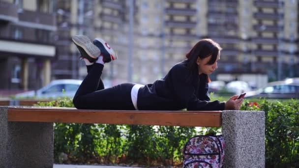 Mujer Joven Acostada Boca Afuera Banco Con Las Piernas Levantadas — Vídeo de stock