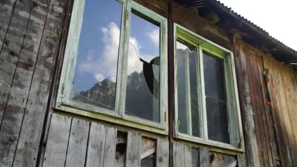 Ventana con cristales rotos en edificio antiguo. Marco de ventana de madera con vidrio parcialmente roto en antiguo edificio de madera abandonado. — Vídeos de Stock