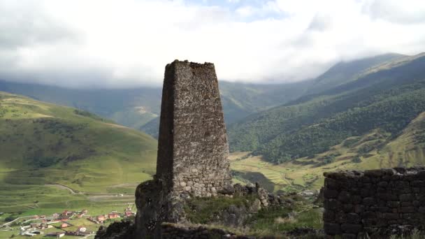 Old stone tower in green mountainous terrain. Ancient stone building of old town located on green hill against mountains covered with forest and fog in summer day — Stock Video