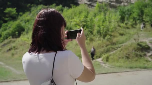 Una joven fotografía la atracción. Una turista toma fotos de las montañas en su teléfono móvil. — Vídeo de stock