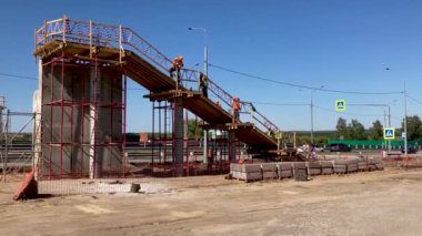 İnşaat işçileri güneşli bir yaz gününde yol üzerinde yaya inşa ediyorlar. İnşaatçılar, açık havada otoyolun yukarısından yaya geçişi yapıyorlar.