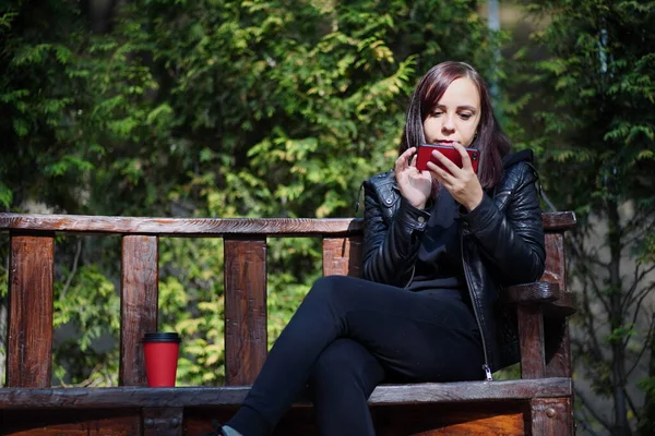 Junge Frau Lederjacke Sitzt Auf Bank Und Spielt Mit Smartphone — Stockfoto