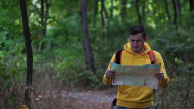 Ormanda haritası olan gezgin bir adam. Sırt çantalı bir adam ormanda yürüyor. Erkek sırt çantası taşıyor ve güneşli sonbahar ormanlarında yürüyor.