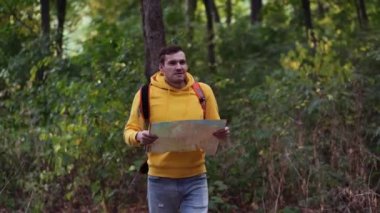 Ormanda haritası olan gezgin bir adam. Sırt çantalı bir adam ormanda yürüyor. Erkek sırt çantası taşıyor ve güneşli sonbahar ormanlarında yürüyor.