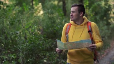Ormanda haritası olan gezgin bir adam. Sırt çantalı bir adam ormanda yürüyor. Erkek sırt çantası taşıyor ve güneşli sonbahar ormanlarında yürüyor.