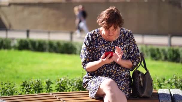 Una donna adulta seduta su una panchina di Park, che guarda il suo cellulare. Una donna che utilizza uno smartphone utilizza Internet nel cortile di un edificio residenziale. — Video Stock