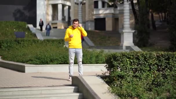 Νεαρός Όμορφος Άντρας Κίτρινη Κουκούλα Μπροστά Από Κτίριο Ακούει Μουσική — Αρχείο Βίντεο